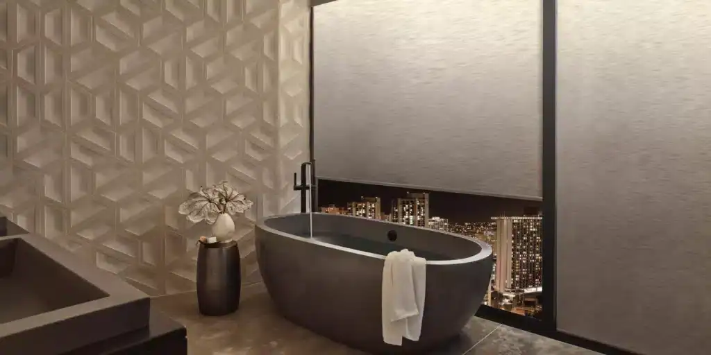 A stylish hotel bathroom featuring a contemporary freestanding bathtub, decorative vase with leaves, and city skyline view through a large window at night. Perfect for a luxurious getaway.